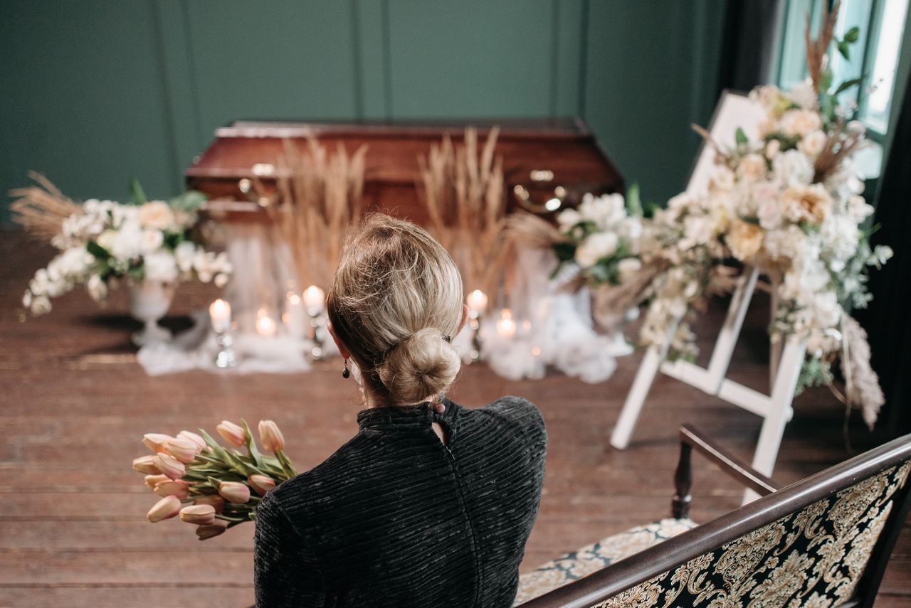 our-mission A woman mourns at an indoor funeral ceremony with floral decorations and a coffin.